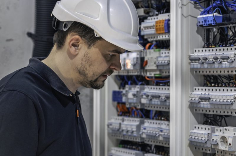 Man, an electrical technician working in a switchboard with fuses. Installation and connection of electrical equipment. Professional uses a tablet.