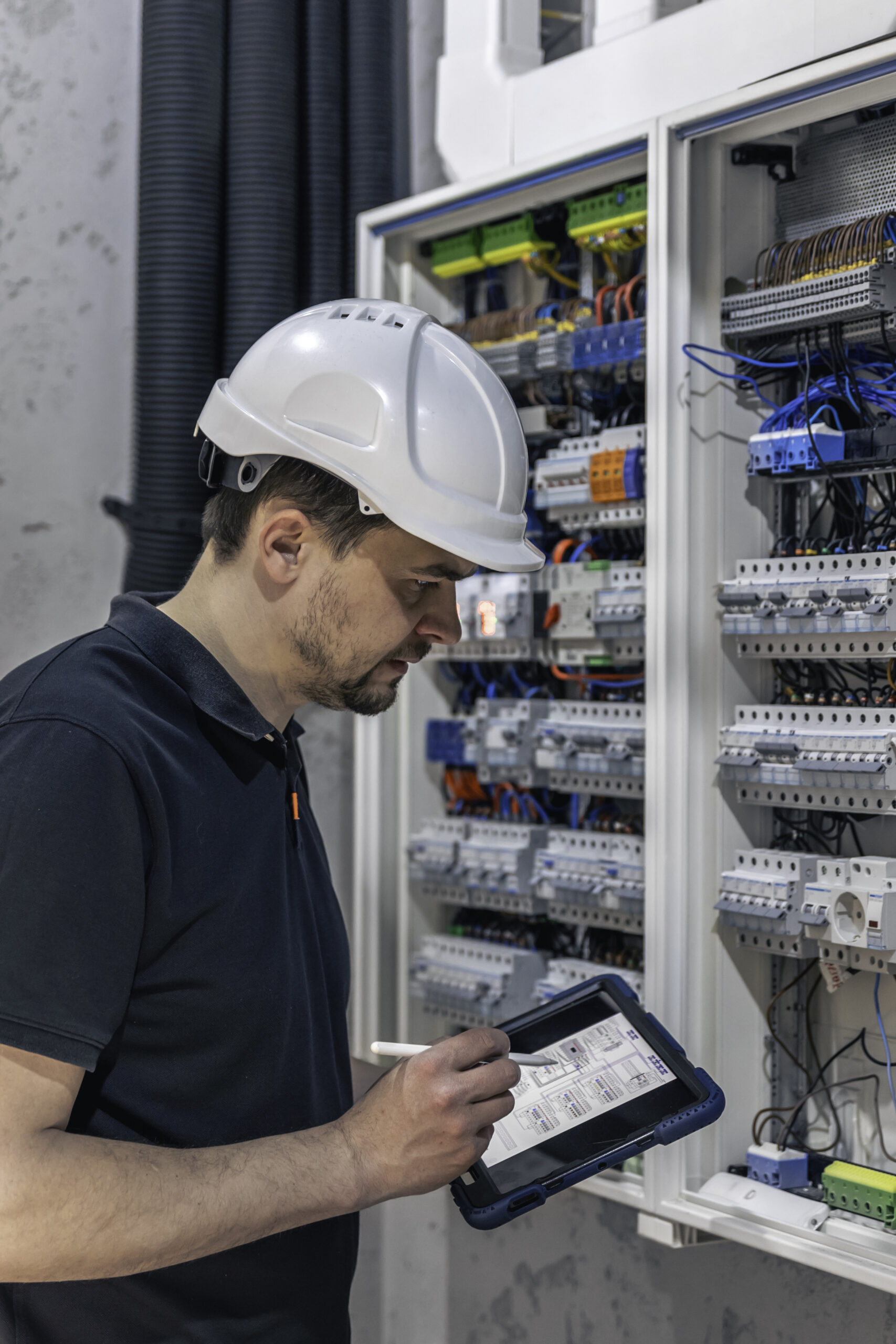 Man, an electrical technician working in a switchboard with fuses. Installation and connection of electrical equipment. Professional uses a tablet.
